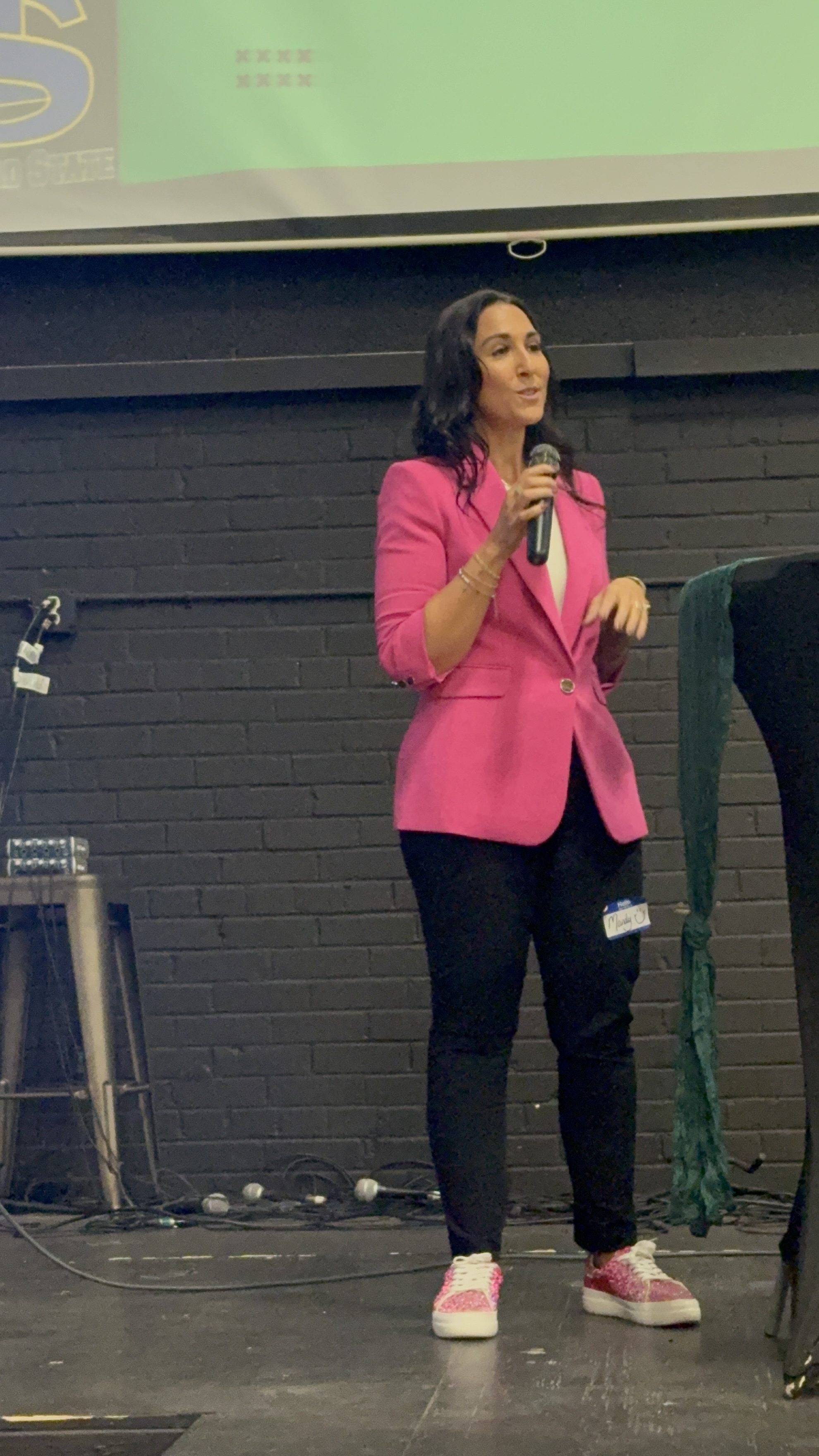 Mandy Reed addressing an audience in a bright pink blazer