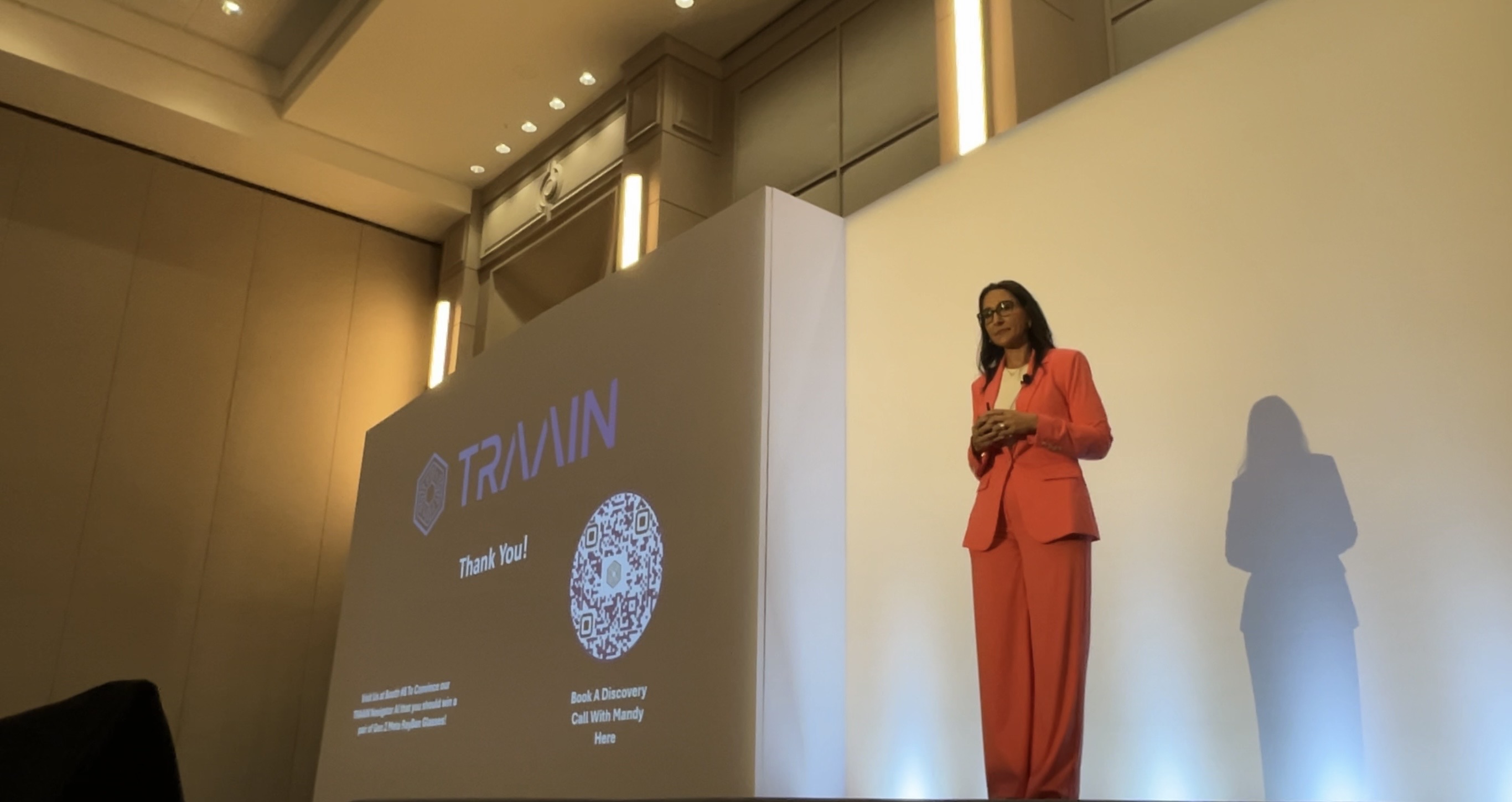 Mandy Reed on a conference stage beside a Traain presentation